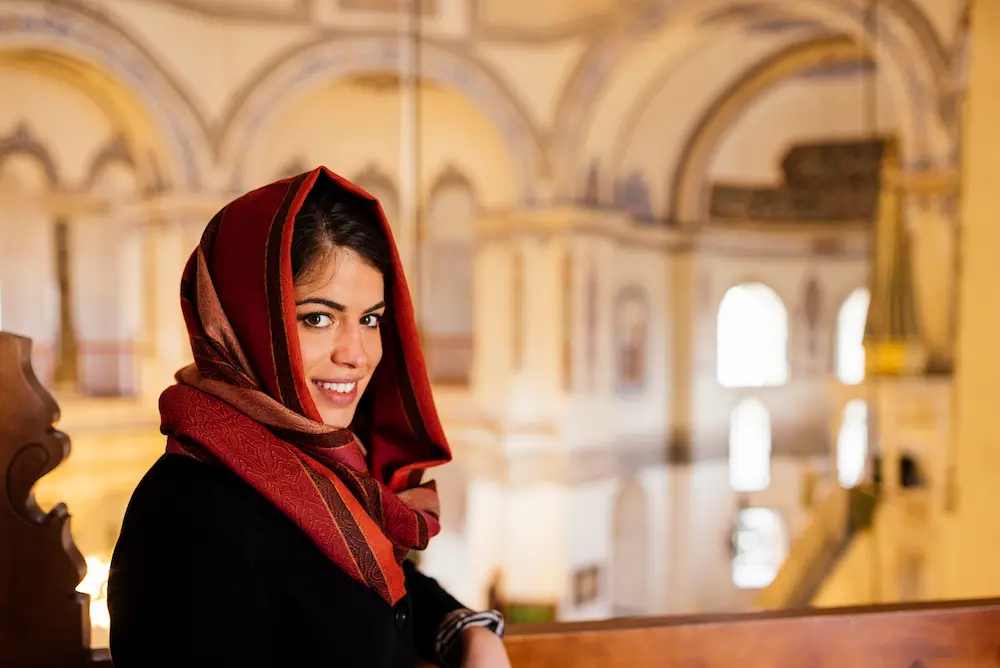 A young Muslim woman drapes a shawl over her head, with some hair visible.